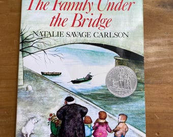 Könnte beinhalten: Ein Vintage-Exemplar von "The Family Under the Bridge" von Natalie Savage Carlson. Das Buchcover zeigt eine Illustration einer Familie, die in der Nähe einer Brücke spaziert, mit einem Hund und Booten im Hintergrund. Der Titel ist rot, der Name des Autors schwarz.