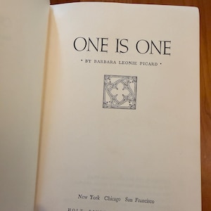 May include: An open book displaying the title "ONE IS ONE" by Barbara Leonie Picard. The page includes a decorative emblem and the publisher's details: Holt, Rinehart and Winston, and the city names.