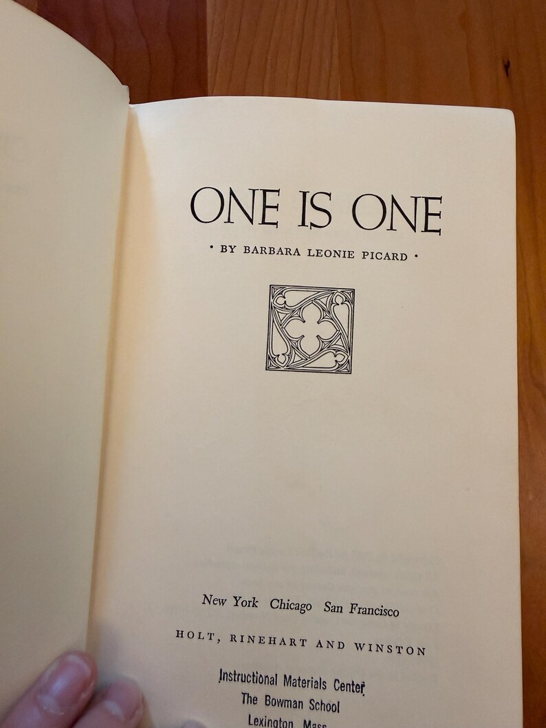 May include: An open book displaying the title "ONE IS ONE" by Barbara Leonie Picard. The page includes a decorative emblem and the publisher's details: Holt, Rinehart and Winston, and the city names.