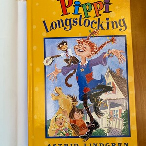 May include: A yellow book cover with a colorful illustration of Pippi Longstocking, a girl with red braids, jumping with a monkey on her shoulder. The book title is "Pippi Longstocking" and the author is "Astrid Lindgren".