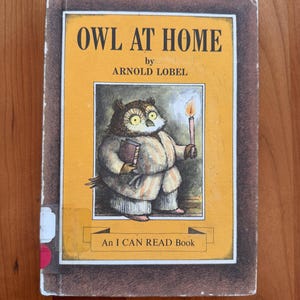Puede incluir: Un libro infantil vintage titulado "OWL AT HOME" de Arnold Lobel. La portada presenta una ilustración de un búho sosteniendo un libro y una vela. El libro forma parte de la serie "An I CAN READ Book".