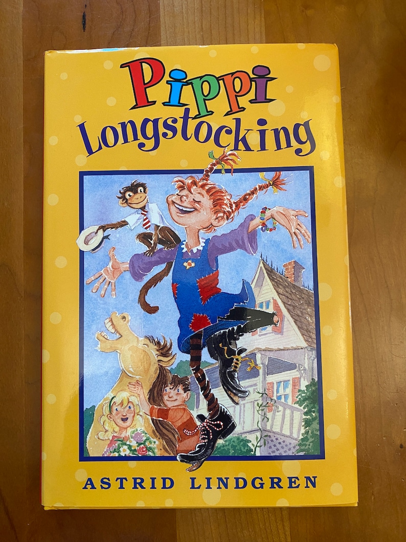 May include: A yellow book cover with a colorful illustration of Pippi Longstocking, a girl with red hair in a blue dress, jumping with a monkey on her shoulder. The book title is "Pippi Longstocking" and the author is "Astrid Lindgren".