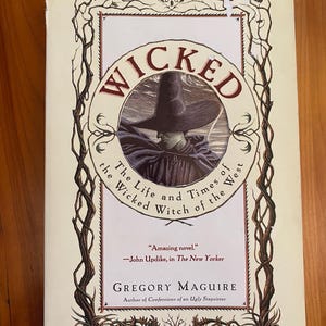 May include: A paperback book titled "WICKED" with a circular illustration of a witch in a hat. The cover features text that reads "The Life and Times of the Wicked Witch of the West" and "More Than 1 Million Copies in Print."