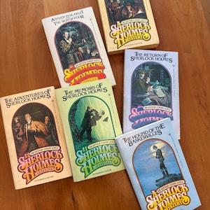 May include: A collection of vintage Sherlock Holmes mystery books. The book covers feature illustrations and titles like "The Case Book of Sherlock Holmes" and "The Hound of the Baskervilles". The books are arranged on a wooden surface.