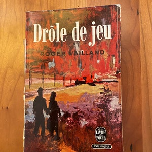 May include: A vintage paperback book titled "Drôle de jeu" by Roger Vailland. The cover features a colorful abstract painting of a couple walking in a landscape with a red sky.