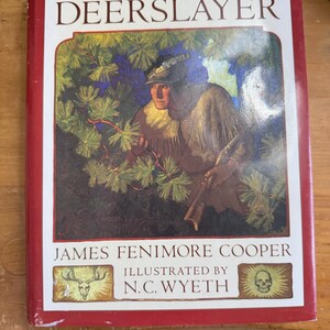 May include: A hardcover book titled "The Deerslayer" by James Fenimore Cooper, illustrated by N.C. Wyeth. The cover features a painting of a man in a forest setting, with text in a white box and a red border.