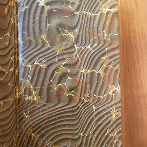 Pu&ograve; includere: Primo piano delle controguardie marmorizzate di un libro in tonalit&agrave; di marrone, oro e bianco. Il motivo marmoreo &egrave; intricato e vorticoso.