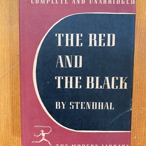 Pode incluir: Uma capa de livro de cor bordô e preta com o título "O Vermelho e o Negro" de Stendhal. O livro faz parte da série The Modern Library.