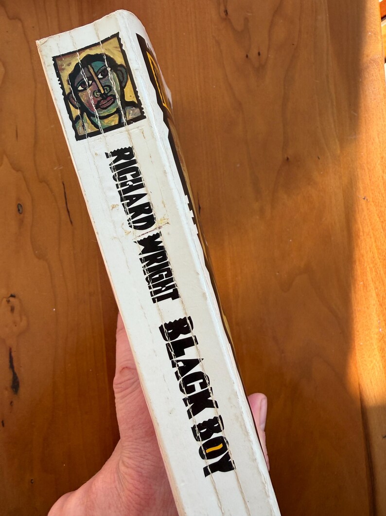 Op de afbeelding: Boekenrug met de titel "Black Boy" van Richard Wright. De omslag toont een portretillustratie met groene, blauwe en gele accenten. De rug is wit met zwarte tekst.