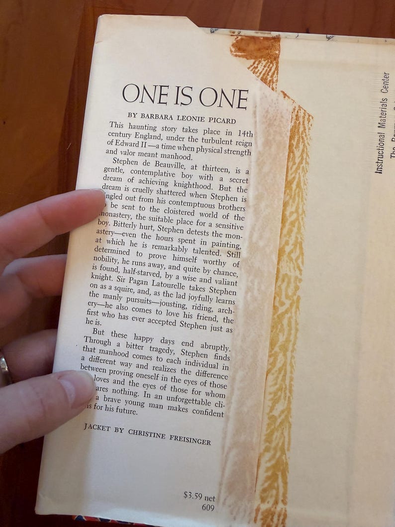 May include: A vintage book titled "One Is One" by Barbara Leonie Picard. The book's cover is partially visible, with text describing the story's setting in 14th-century England. The jacket is designed by Christine Freisinger.