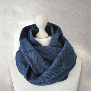 Könnte beinhalten: Blauer Loop-Schal aus strukturiertem Strickstoff. Der Schal ist um einen weißen Mannequinkopf und Schultern drapiert. Die Farbe des Schals ist ein gedämpftes, mittleres Blau, und das Strickmuster ist sichtbar.