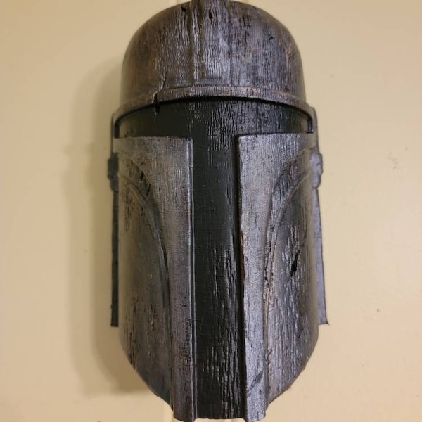 Op de afbeelding: Een verweerde helm met een metallic uitstraling en een donkere verticale streep in het midden. De helm heeft een afgeronde bovenkant en hoekige elementen, met zichtbare textuur en een versleten afwerking, wat een gevechtsklare uitstraling suggereert. Het ontwerp roept een sciencefiction- of fantasiethema op.