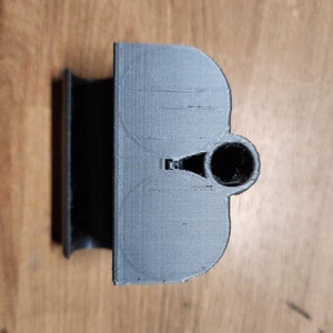 Puede incluir: Un objeto gris impreso en 3D con una parte superior redondeada y un agujero cil&iacute;ndrico. El objeto tiene una base rectangular y un dise&ntilde;o curvo semicircular. La superficie tiene l&iacute;neas de capa visibles.