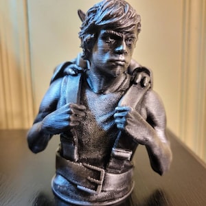 May include: A 3D printed bust of a fictional character, a young man with short brown hair, wearing a dark grey shirt and a belt. He is carrying a smaller figure on his back.
