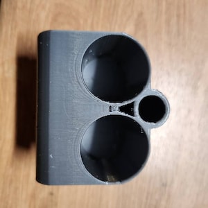 Puede incluir: Un objeto gris impreso en 3D con tres aberturas circulares de diferentes tama&ntilde;os. El objeto parece ser un soporte o organizador, posiblemente para objetos peque&ntilde;os. El material tiene l&iacute;neas de capa visibles del proceso de impresi&oacute;n.