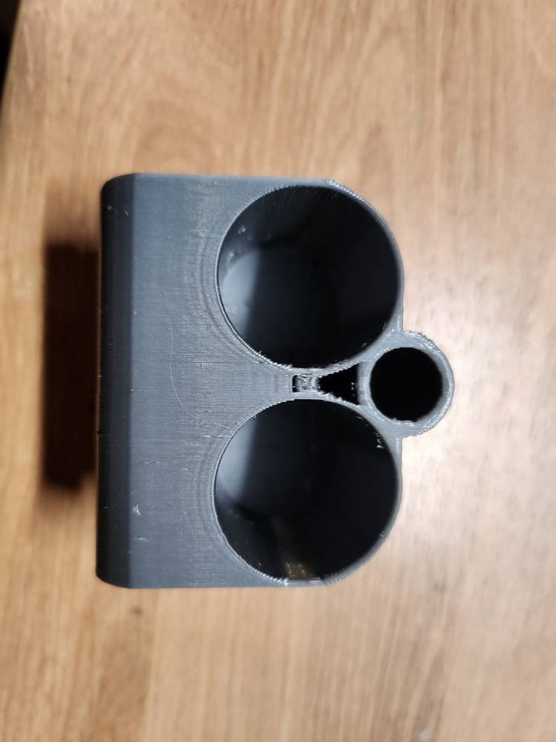 Puede incluir: Un objeto gris impreso en 3D con tres aberturas circulares de diferentes tama&ntilde;os. El objeto parece ser un soporte o organizador, posiblemente para objetos peque&ntilde;os. El material tiene l&iacute;neas de capa visibles del proceso de impresi&oacute;n.