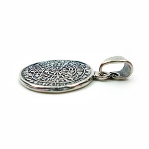 May include: Silver pendant with a circular design featuring intricate details and a loop for attaching to a chain.