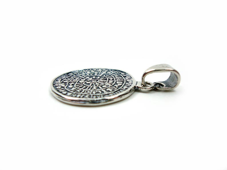 May include: Silver pendant with a circular design featuring intricate details and a loop for attaching to a chain.