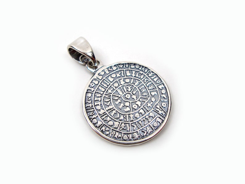 May include: Silver pendant with a circular design featuring a spiral pattern and symbols around the edge.