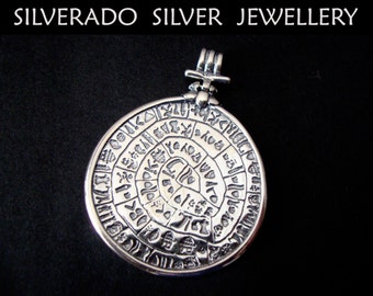 May include: A silver pendant featuring a circular design with intricate engravings. The pendant has a loop at the top for attaching to a chain.