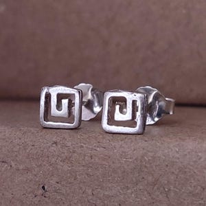 Puede incluir: Un par de pendientes de plata con un diseño cuadrado que presenta un patrón geométrico.