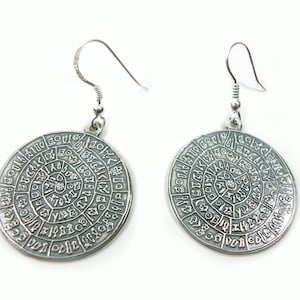 Pode incluir: Brincos de prata com um design circular que apresenta uma espiral de símbolos e letras. Os brincos têm um fecho simples de gancho.