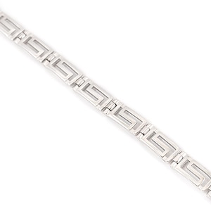 May include: A silver-colored bracelet with a repeating Greek key design. The bracelet is made of connected rectangular links, each featuring a geometric pattern. The links are flat and have a polished finish, reflecting light.