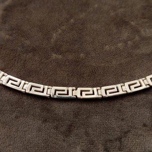 May include: A silver chain necklace with a Greek key pattern.