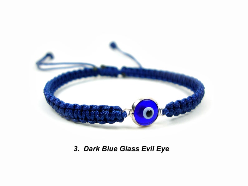 May include: A dark blue braided bracelet with a dark blue glass evil eye charm. The charm has a white center and a silver rim.