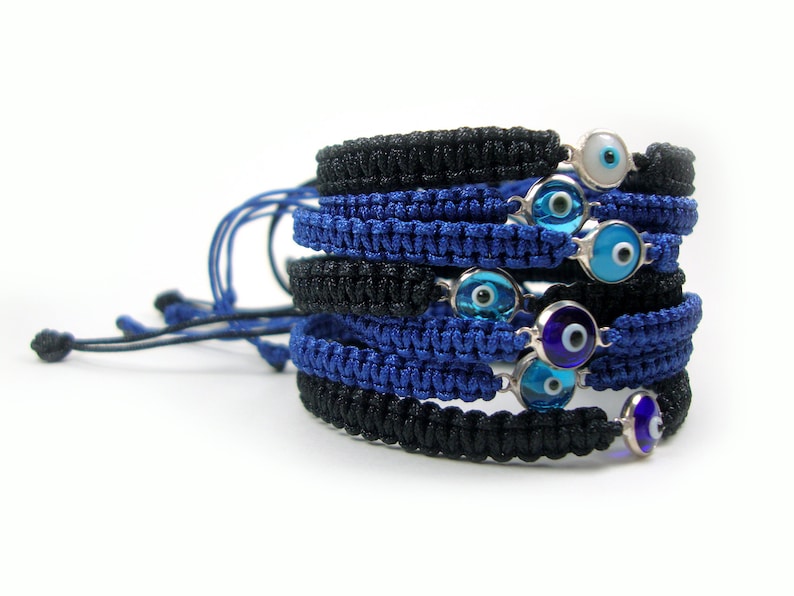 May include: A stack of blue and black braided bracelets with silver charms featuring blue evil eyes.