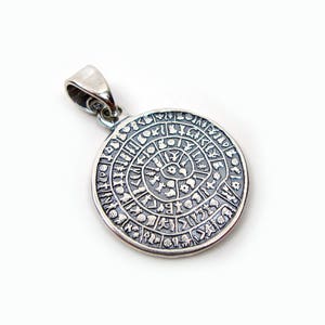 May include: Silver pendant with a circular design featuring a spiral pattern and symbols around the edge.