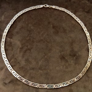 May include: A silver chain necklace with a Greek key pattern.