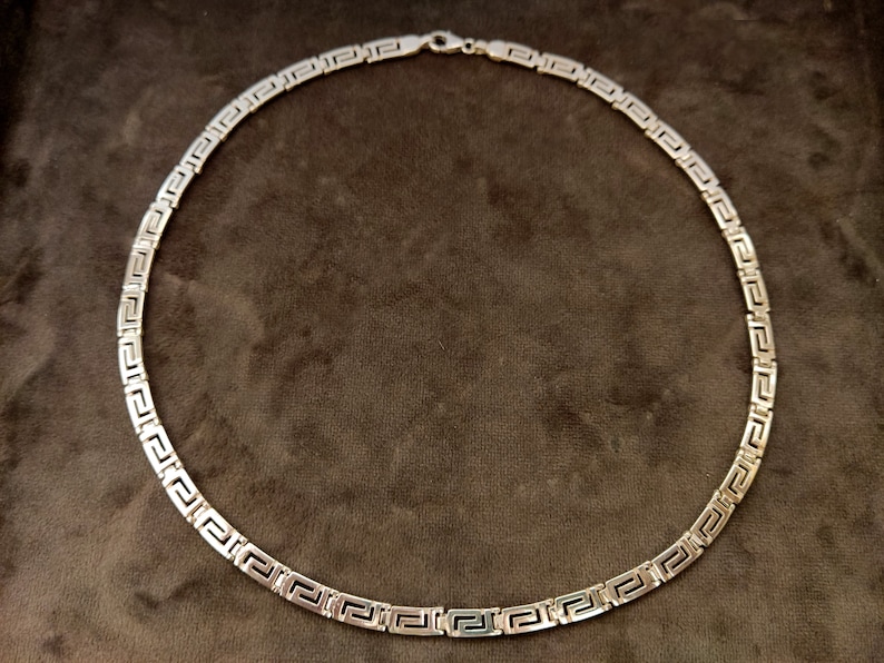 May include: A silver chain necklace with a Greek key pattern.