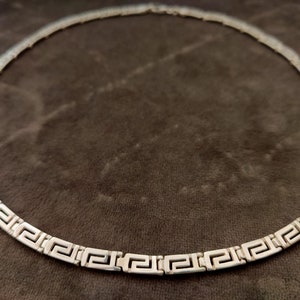 May include: A silver necklace with a Greek key pattern.