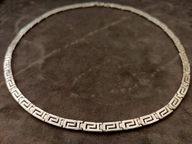 May include: A silver necklace with a Greek key pattern.