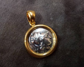 May include: A gold-toned pendant with a circular coin design. The coin features a profile of a person with a detailed hairstyle. The pendant has a gold loop for a chain. The coin is silver-toned with a gold border.
