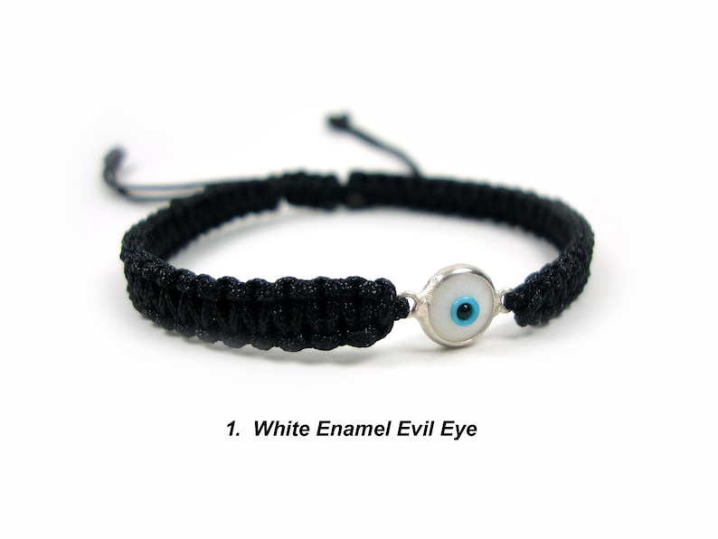May include: Black braided bracelet with a white enamel evil eye charm. The charm has a blue center.