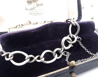 May include: A silver chain bracelet with a lobster clasp and a small safety chain. The bracelet is in a black velvet box with a white label that says "Kendal & Dent".