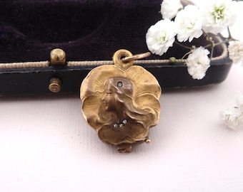 May include: A gold-toned metal pendant featuring a relief sculpture of a profile of a person with long flowing hair. The design includes a small embedded stone in the hair and three tiny stones arranged in a row at the base of the neck.