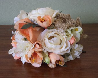 May include: A bridal bouquet with peach, white, and cream flowers, accented with burlap ribbon and pearl accents.