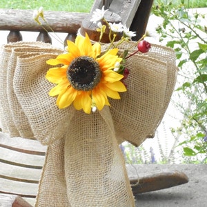 Peut inclure: Un nœud en toile de jute avec un tournesol jaune et des baies rouges, attaché à une chaise en bois.