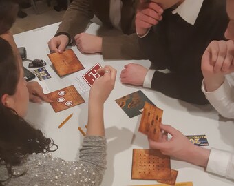May include: Four people are gathered around a table playing a board game. The game includes a wooden board with a grid of holes, wooden pegs, and cards with numbers on them. The people are looking at the board and the cards, and they are concentrating on the game.