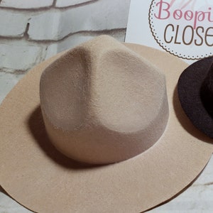 May include: A beige felt fedora hat with a wide brim and a slightly pointed crown.
