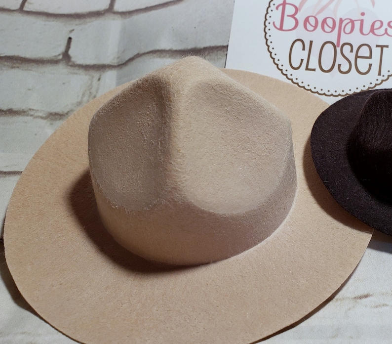 May include: A beige felt fedora hat with a wide brim and a slightly pointed crown.