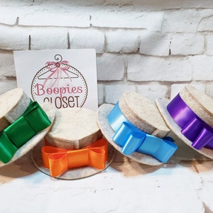 May include: Four felt hats with different colored ribbon bows. The hats are white with a green, orange, blue, and purple ribbon bow.