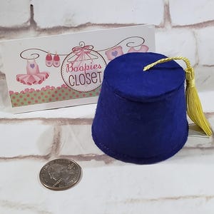May include: A small blue fez hat with a gold tassel. The fez is made of felt and has a flat top. The tassel is attached to the top of the fez and hangs down the side.