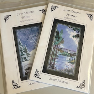 May include: Two art prints titled "Four Seasons" by Bonnie Kaster. One depicts a winter scene with snow-covered trees and a bare tree. The other shows a summer landscape with a lake and trees. Both are in plastic sleeves.