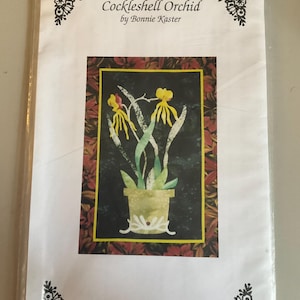 May include: A white paper with the text "Cockleshell Orchid by Bonnie Kaster" and a colorful illustration of an orchid in a pot. The illustration is framed with a red and black border. The text "Sweet Memories" is at the bottom.
