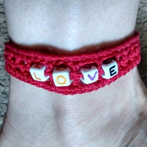Könnte beinhalten: Rotes gehäkeltes Armband mit weißen Perlen, die das Wort "LOVE" in bunten Buchstaben buchstabieren.
