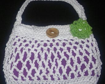Könnte beinhalten: Weiße gehäkelte Handtasche mit lila Futter, einem Holzknopf und einer grünen gehäkelten Blume.